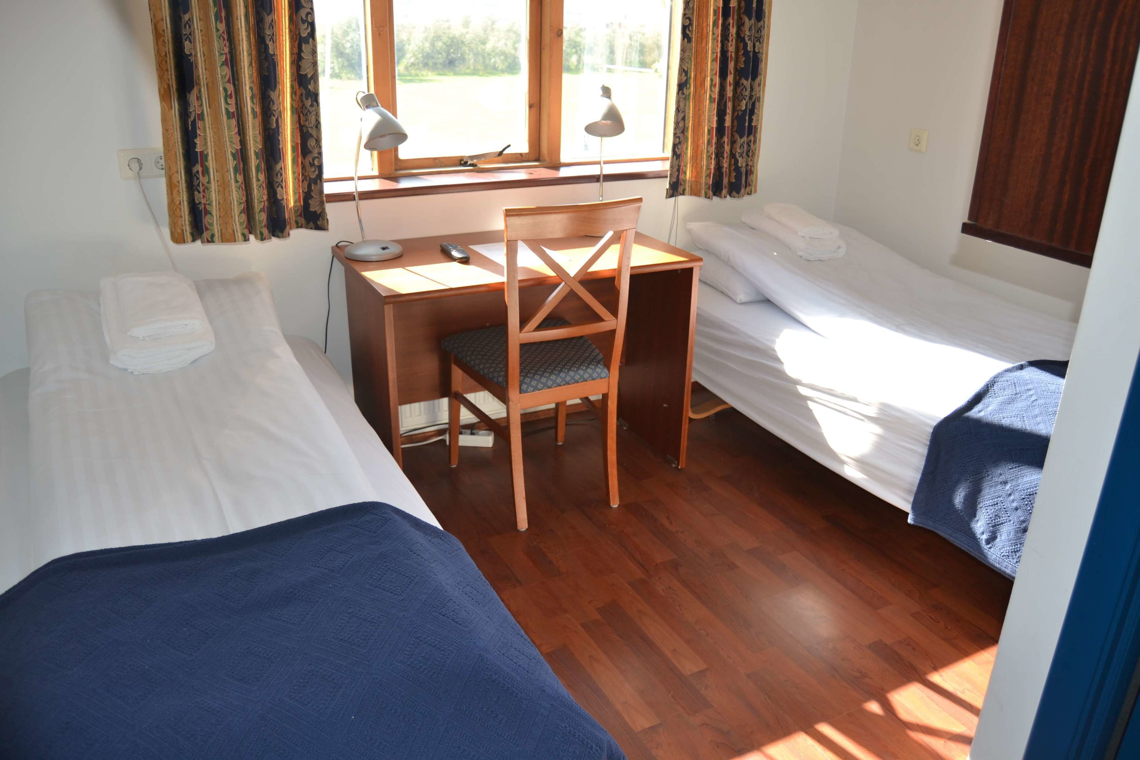 A room with two single beds, a desk with a chair, and a window with curtains.