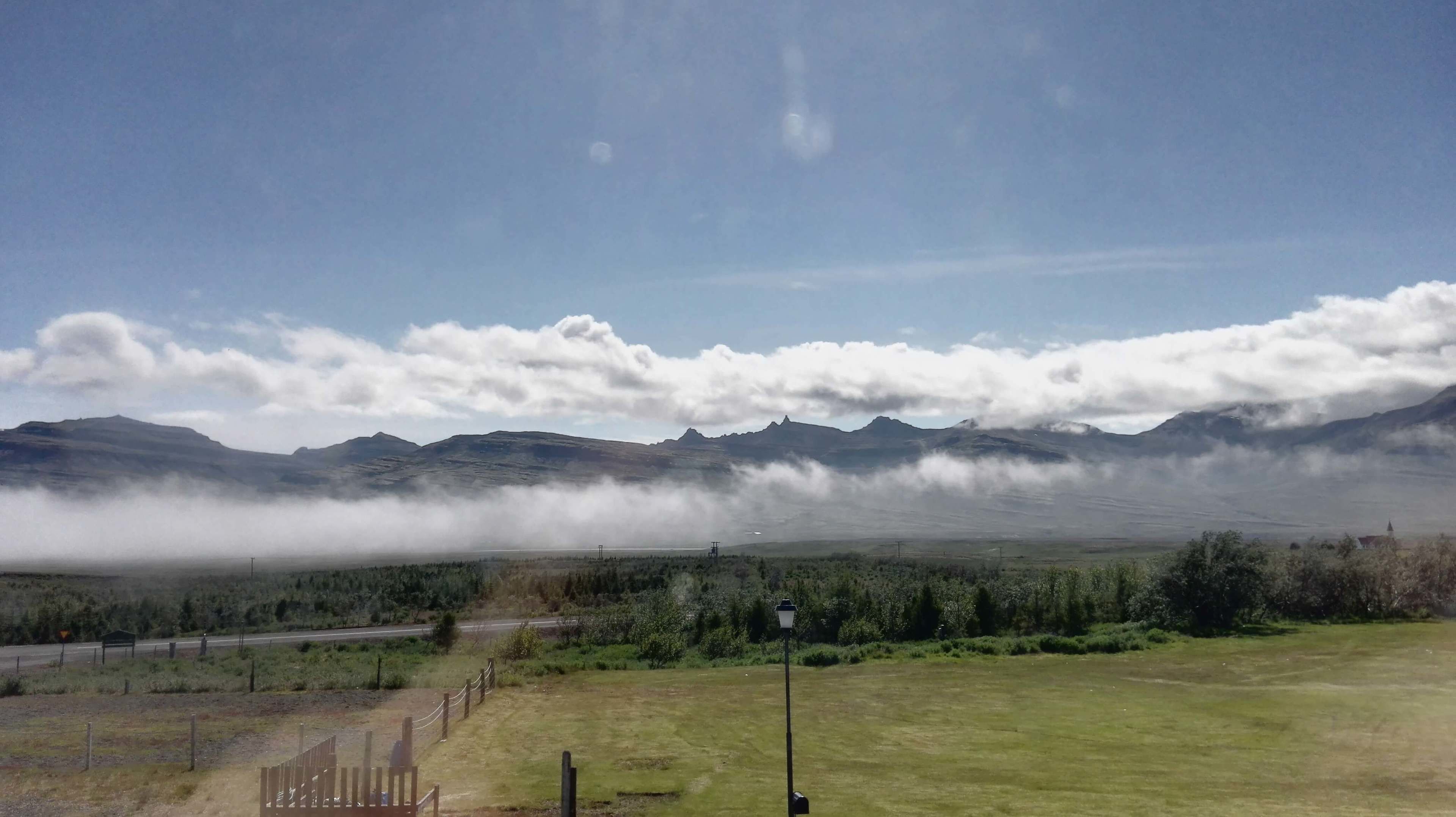A rural landscape with mountains, a road, and a grassy field.