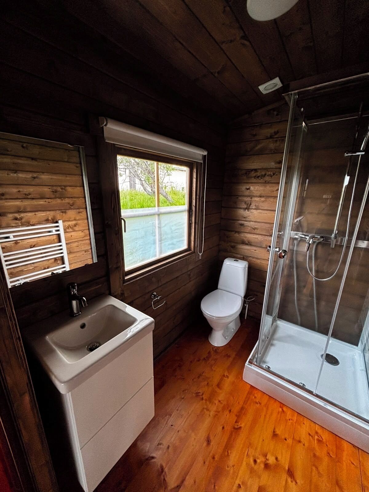 A wooden cabin bathroom with a sink, toilet, and shower.