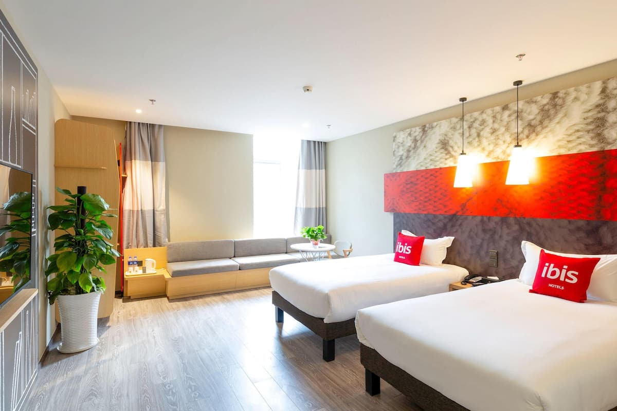 Une chambre d’hôtel avec deux lits, un canapé, un coin repas et une grande fenêtre.