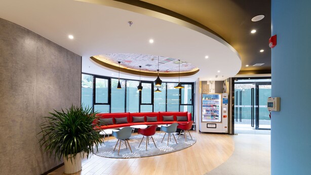 Een moderne lobby met een gebogen plafond, een rode zithoek en een automaat.