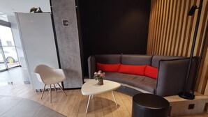A modern living area with a grey sofa, red cushions, a white chair, a small round table, and a black ottoman. - Ibis Xi'an Jianzhang Road Fengdong New Area Hotel (Xi'an)