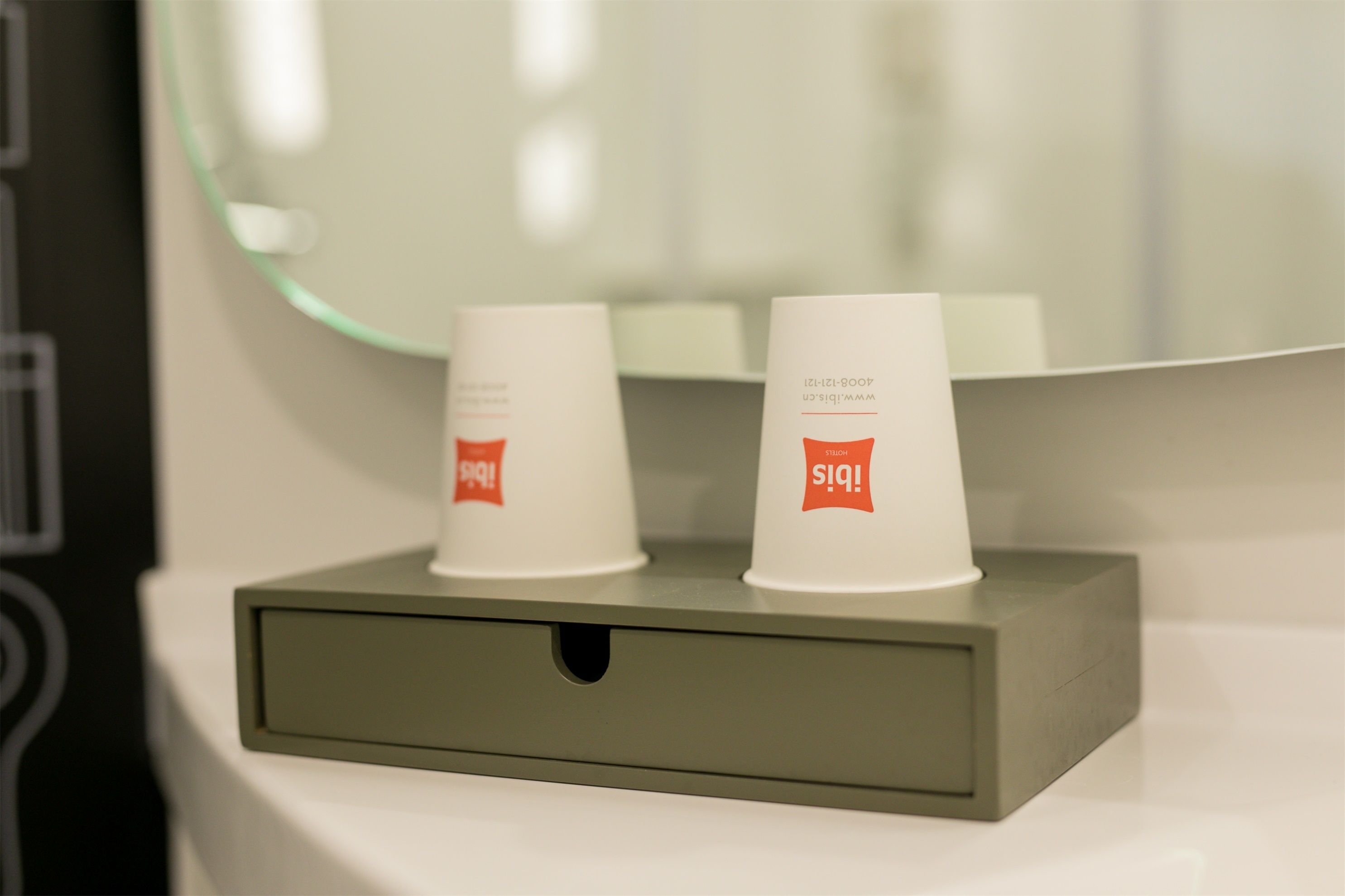 Une salle de bain avec un miroir, deux tasses blanches ornées de logos rouges et un comptoir gris.