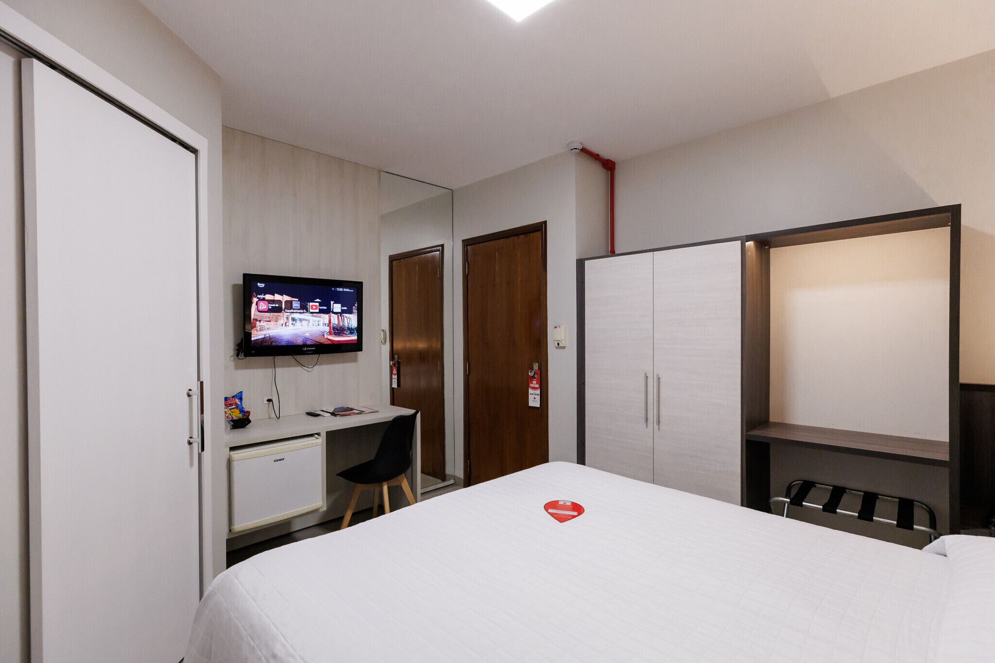A hotel room with a bed, a desk, a chair, a television, and a wardrobe.