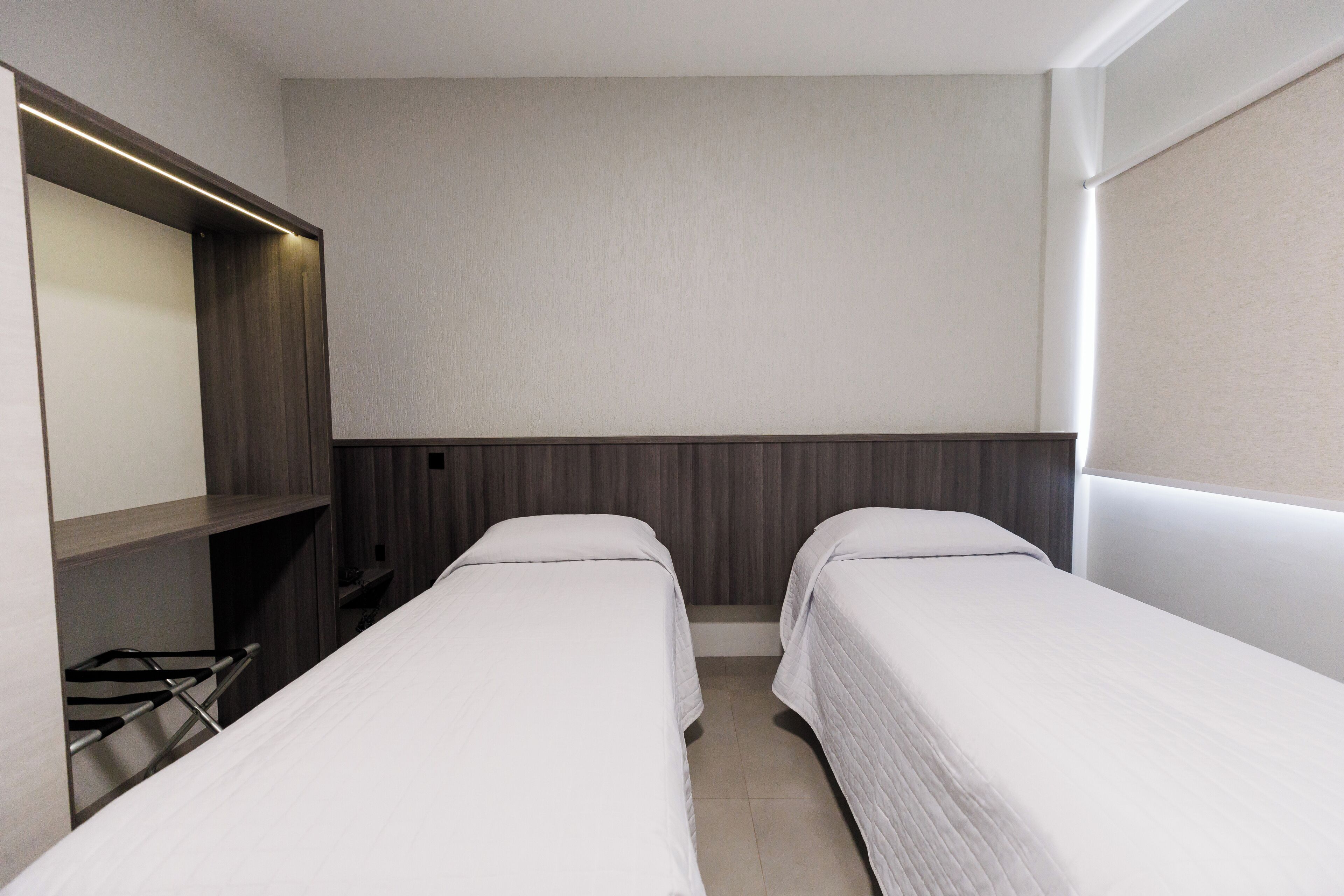 A hotel room with two single beds, a built-in TV, and a wardrobe.
