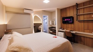 Une chambre d’hôtel avec un lit, un bureau, un téléviseur affichant le logo « NETFLIX », et une salle de bain visible à travers une arche.