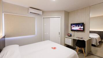 A hotel room with a bed, a desk with a chair, a television, and a wardrobe.