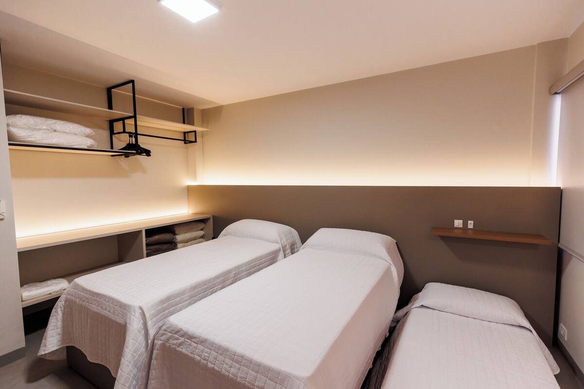 Une chambre d’hôtel avec deux lits simples, une étagère intégrée où sont pliées les serviettes et une table de chevet.