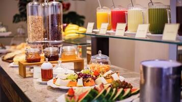 Un bufé con diversos alimentos y bebidas, incluyendo frutas, quesos y una variedad de refrescos.