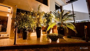 L’entrée d’un hôtel, agrémentée de grands pots de plantes, dotée d’une façade bien éclairée et d’une enseigne bien visible.