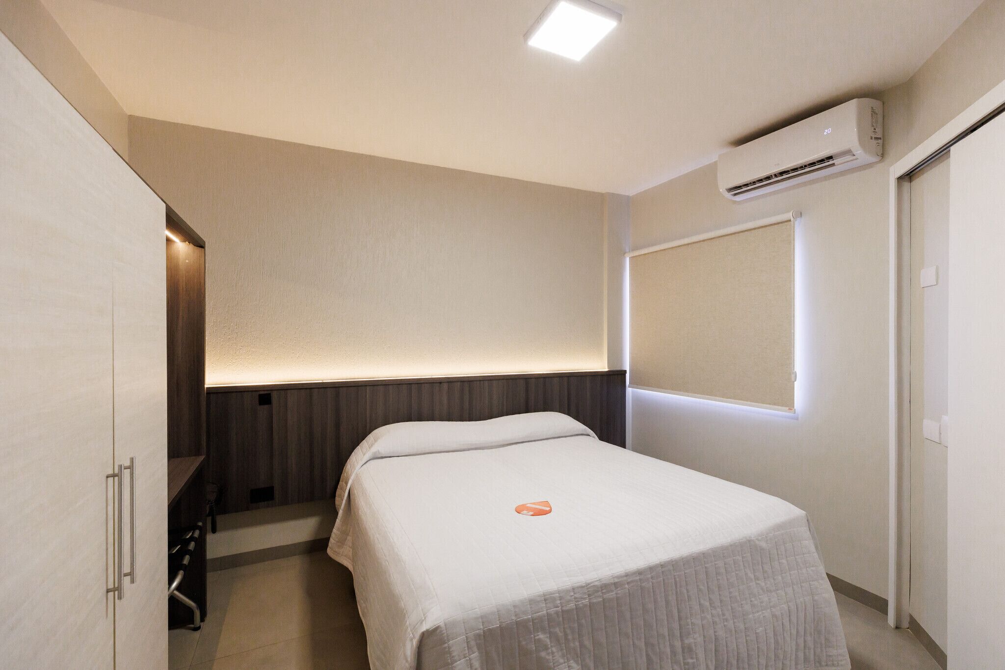 A hotel room with a bed, a desk, a wardrobe, and an air conditioning unit.