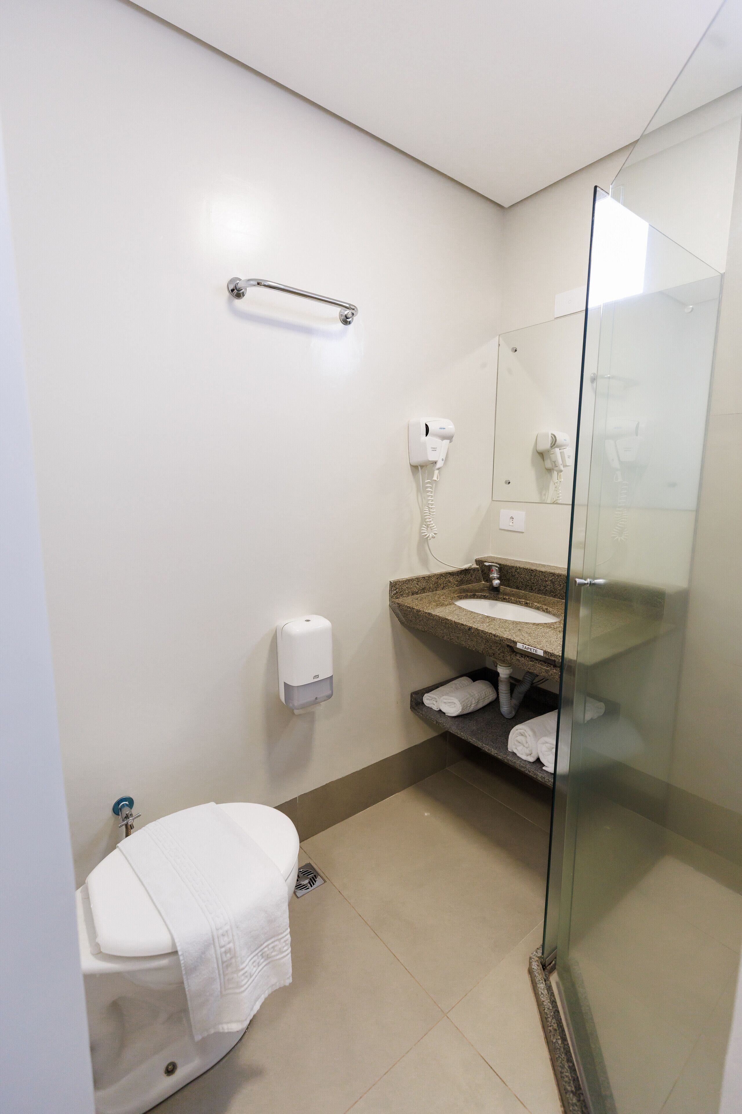 Uma casa de banho moderna com sanita, lavatório, cabine de duche em vidro, um porta-toalhas e secador de cabelo.