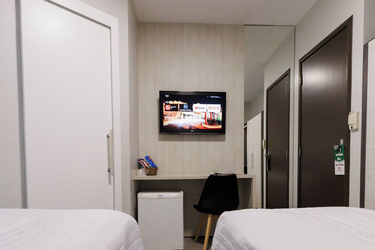 Une chambre d’hôtel avec deux lits, un petit bureau avec une télévision, un réfrigérateur et un miroir.