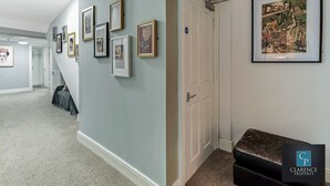 A hallway with framed pictures on the wall, a door, and a bench. - Crawford Apt (Londonderry)