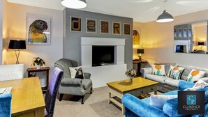 A modern living room with a fireplace, grey and blue sofas, a wooden coffee table, and a framed artwork on the wall. - Crawford Apt (Londonderry)