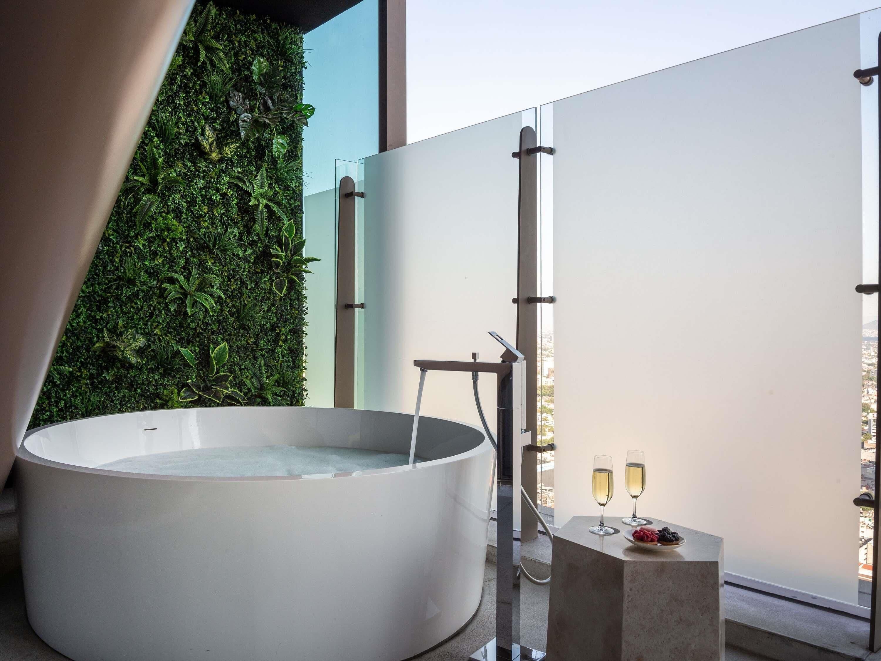 A modern bathroom with a large bathtub, a glass shower enclosure, and a balcony with a city view.