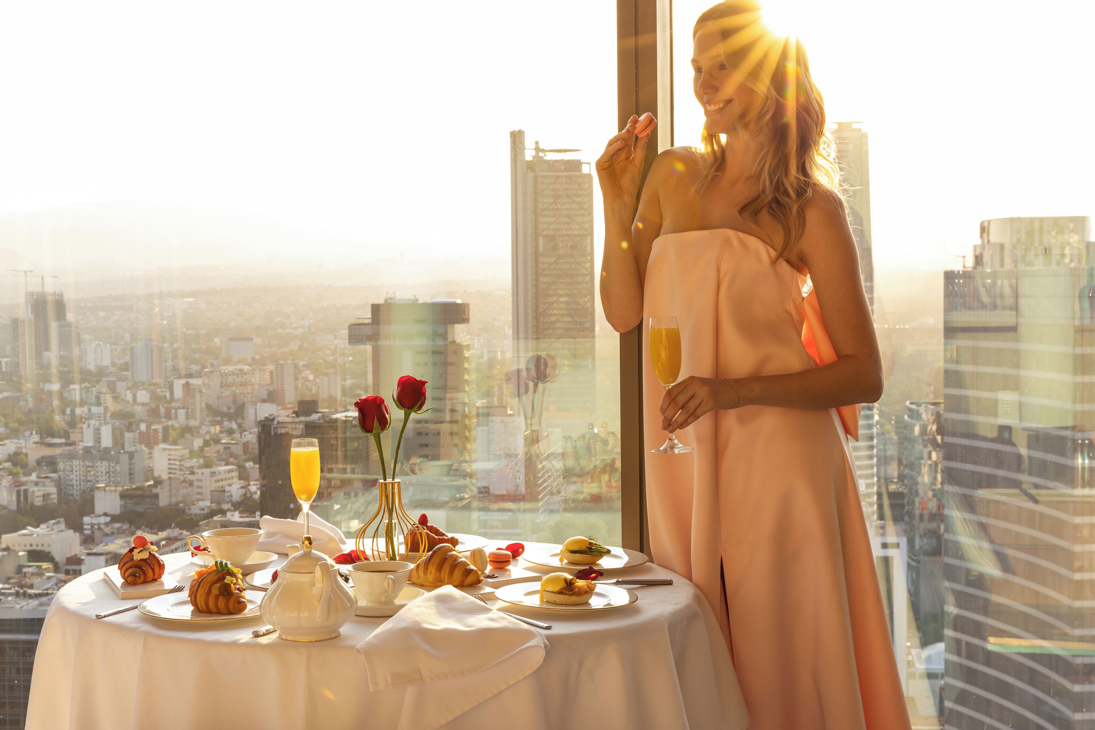 A table set with breakfast items and a glass of orange juice, with a cityscape view in the background.