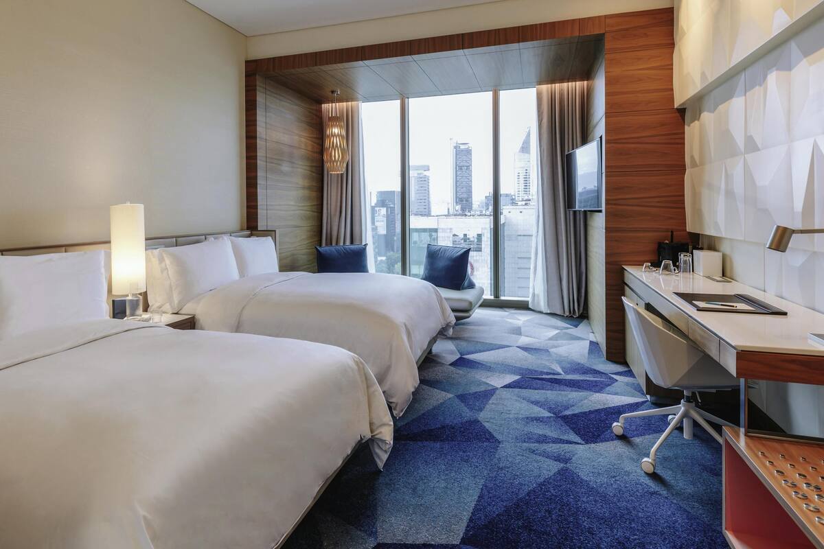 Une chambre d’hôtel avec deux lits, un bureau, une chaise, une télévision et une vue sur la ville.