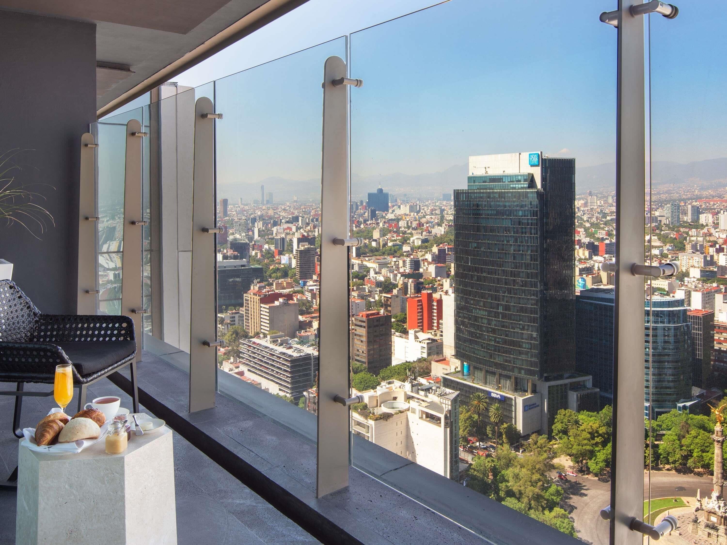 Een balkon met uitzicht op de stad, een stoel, een tafel met croissants, koffie en sap, en een glas sinaasappelsap.