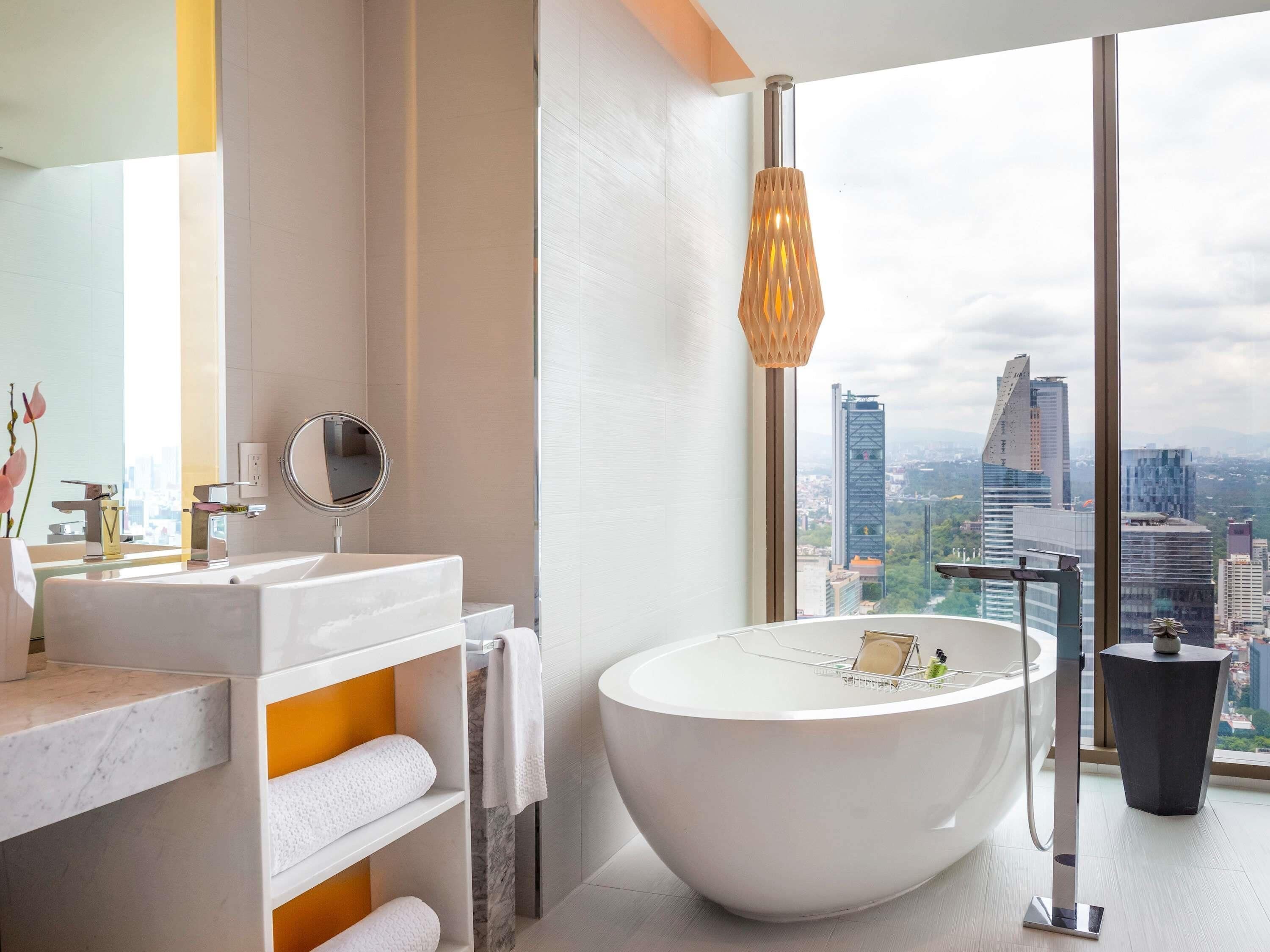 A modern bathroom with a large bathtub, a vanity with a mirror, and a view of a cityscape through large windows.