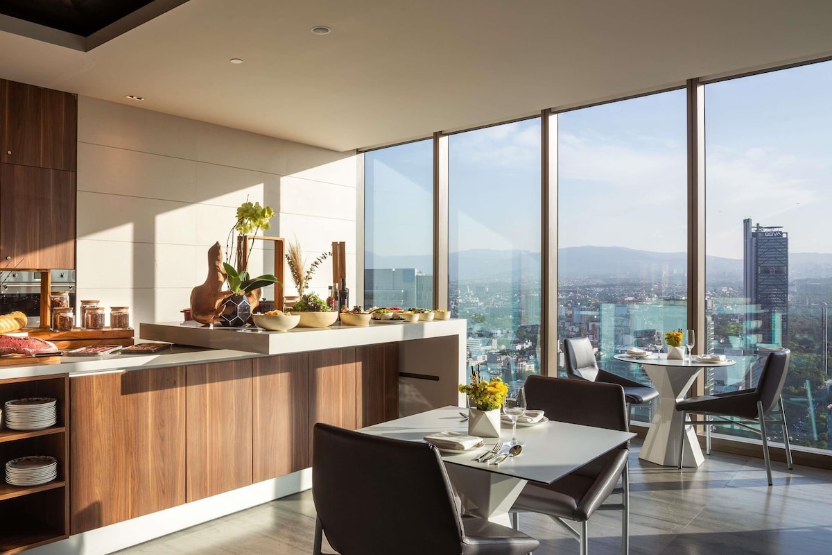 Una cocina moderna con vistas a la ciudad, un comedor con una mesa dispuesta para dos personas y un amplio ventanal.