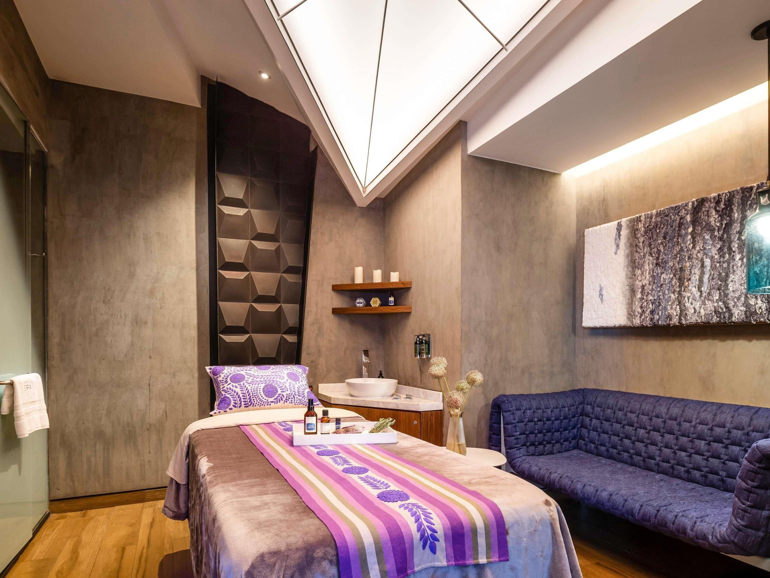 A modern bedroom with a bed, a sofa, a vanity with a mirror, and a wall-mounted shelf.