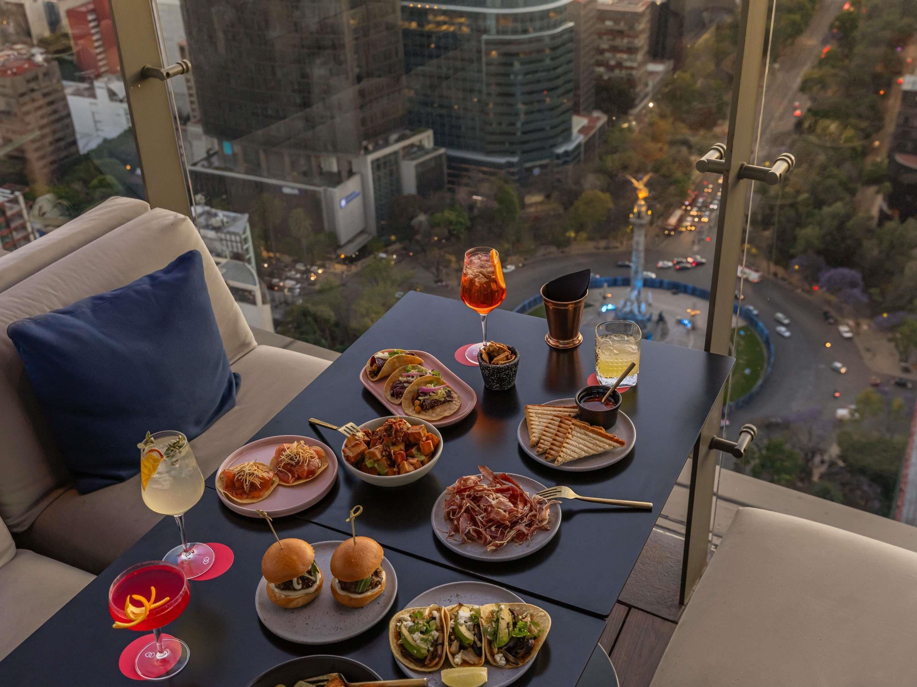 A table set with various dishes and drinks, overlooking a cityscape.