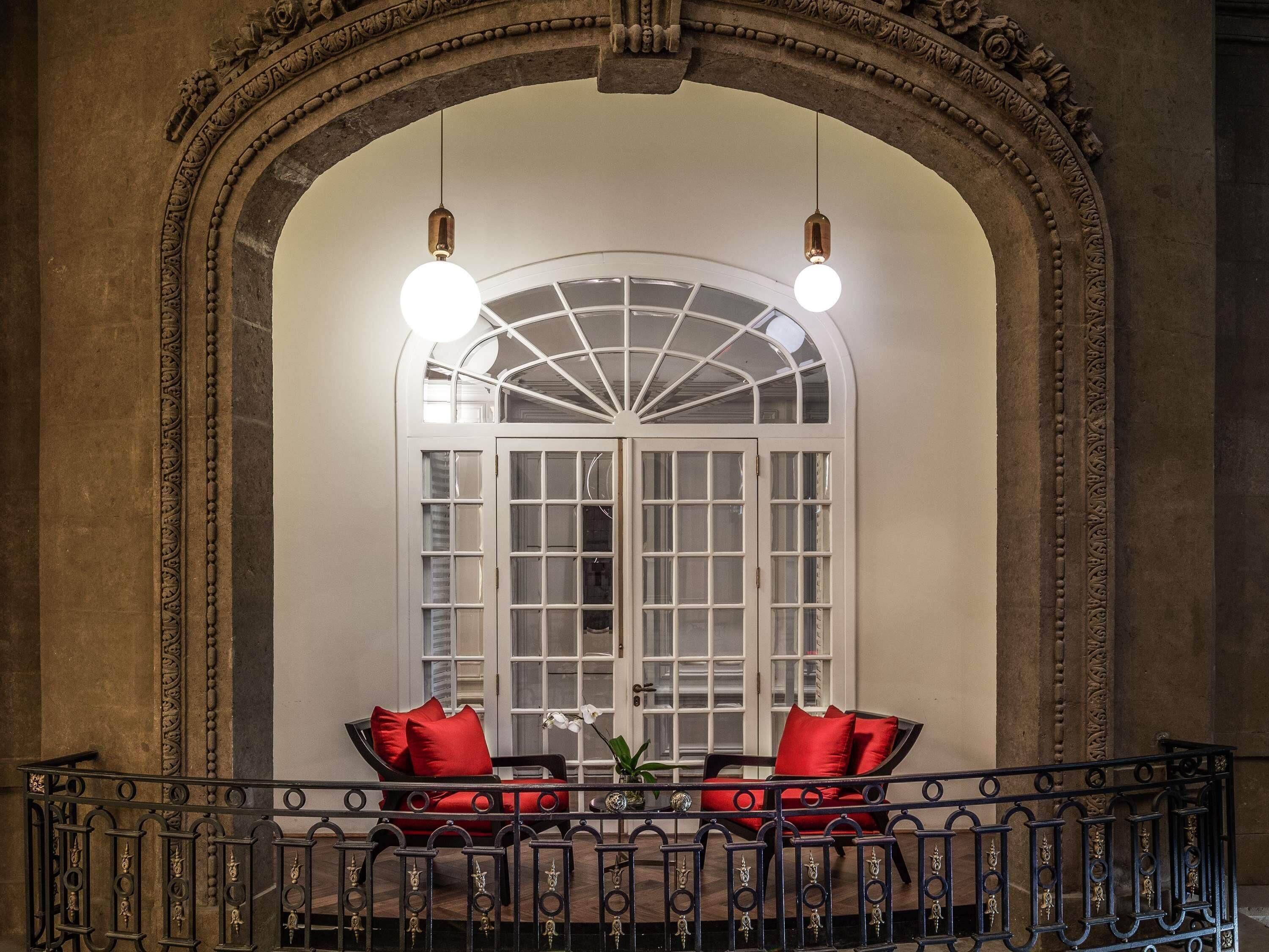 A room with a large arched doorway, a window with multiple panes, and two chairs with red cushions.