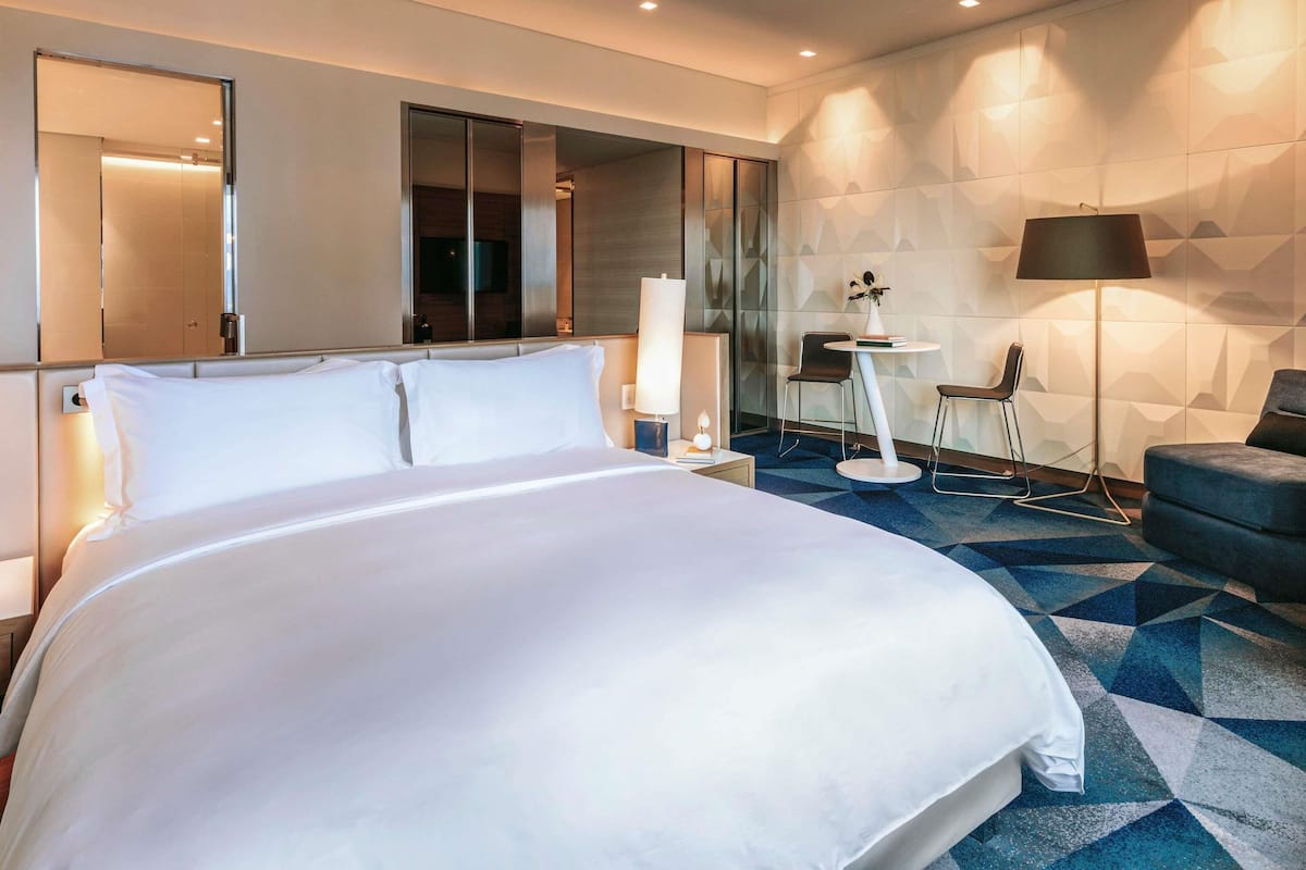 Une chambre d’hôtel moderne avec un grand lit, un bureau avec une chaise, une lampe et un miroir.
