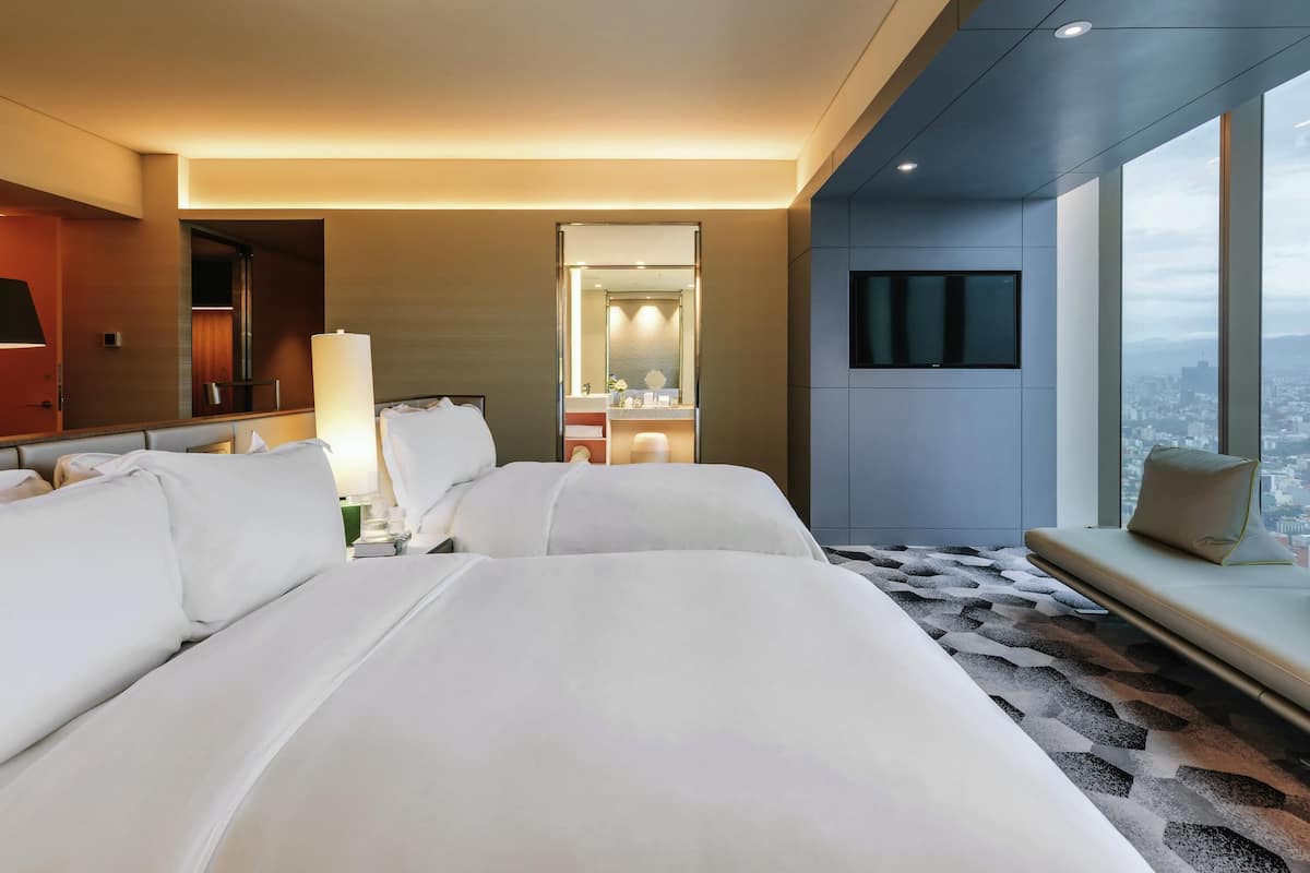 Une chambre d’hôtel avec deux lits, un grand miroir, une télévision et une vue sur la ville.