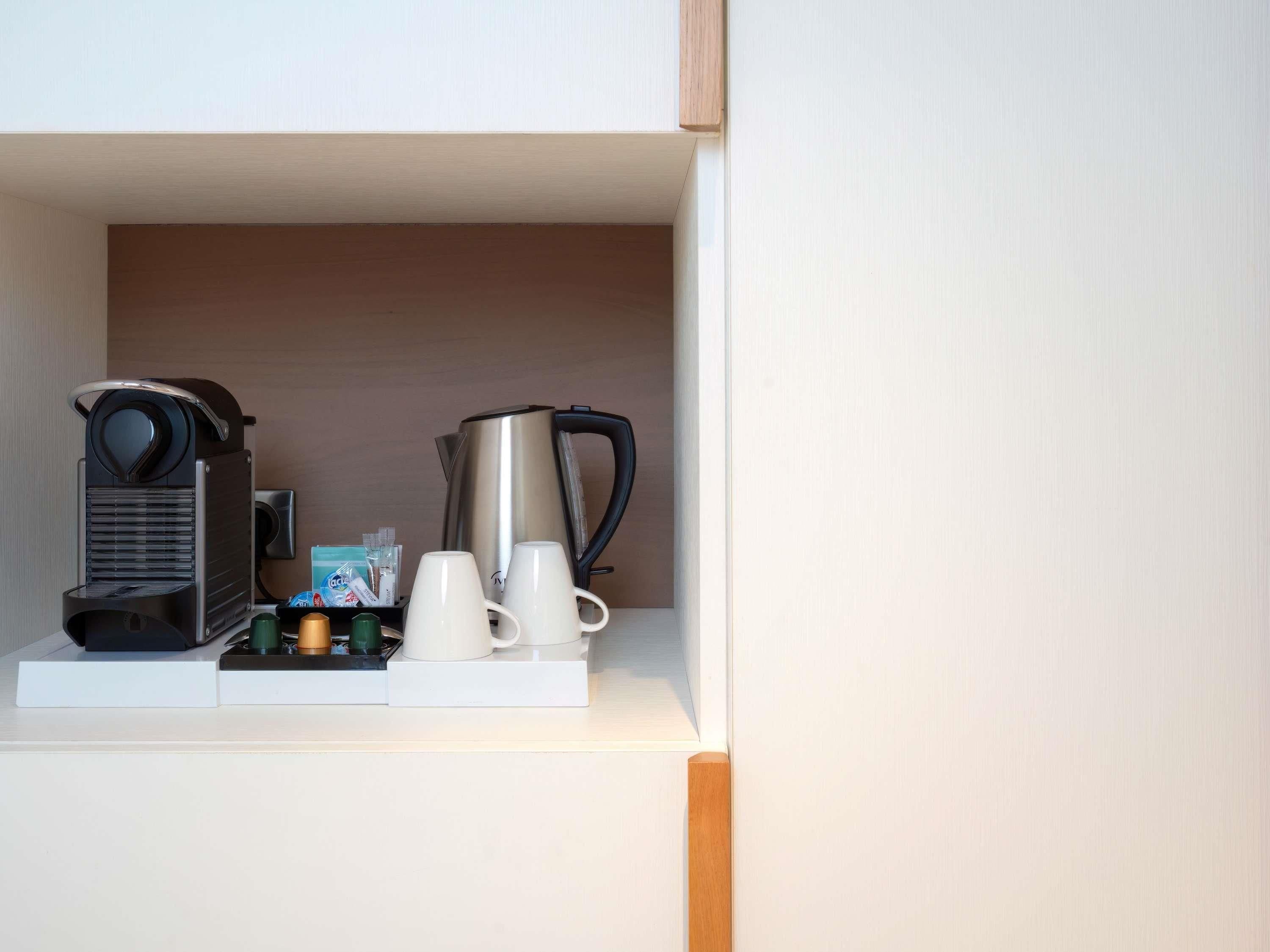 Una estación de café con una cafetera, un hervidor y dos tazas sobre una encimera blanca.