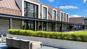Un bâtiment moderne doté d’un toit plat, de grandes fenêtres et d’un espace extérieur couvert comprenant un canapé et une table.