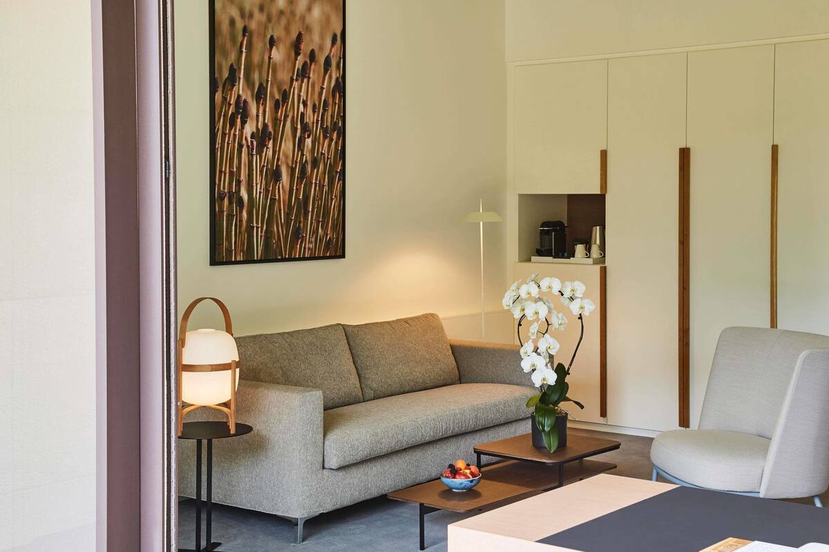 Ein modernes Wohnzimmer mit einer Couch, einem Couchtisch, einem Sessel, einer Lampe und einer Vase mit weißen Blumen.