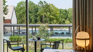 A modern room with a view of a pool and greenery. It includes a table with chairs, a lamp, and a book. - Le Domaine des Vanneaux Golf & Spa L'Isle Adam - MGallery Collection (Presles)