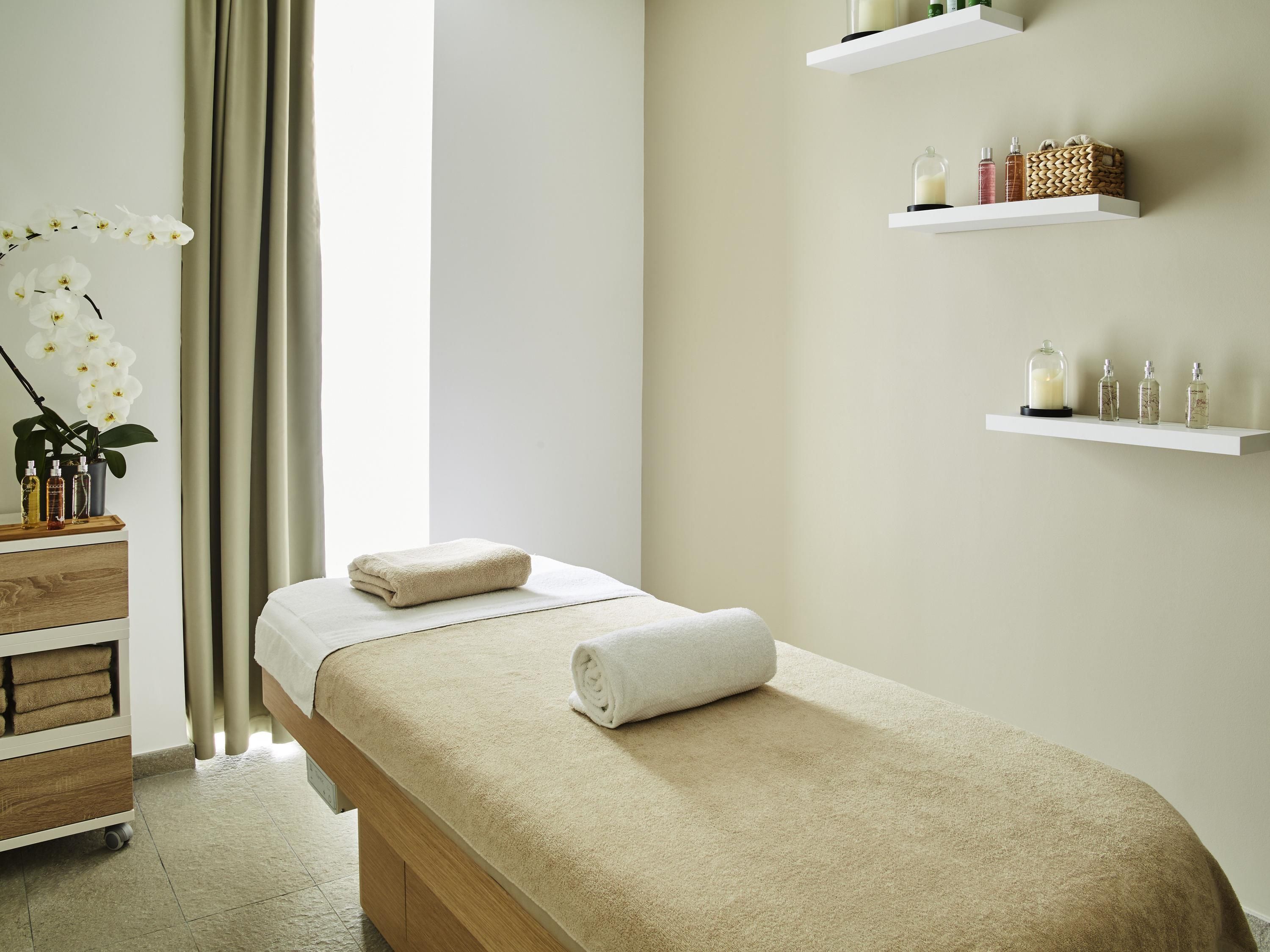 Une salle de spa équipée d’une table de massage, d’étagères contenant des produits de toilette et d’une plante.