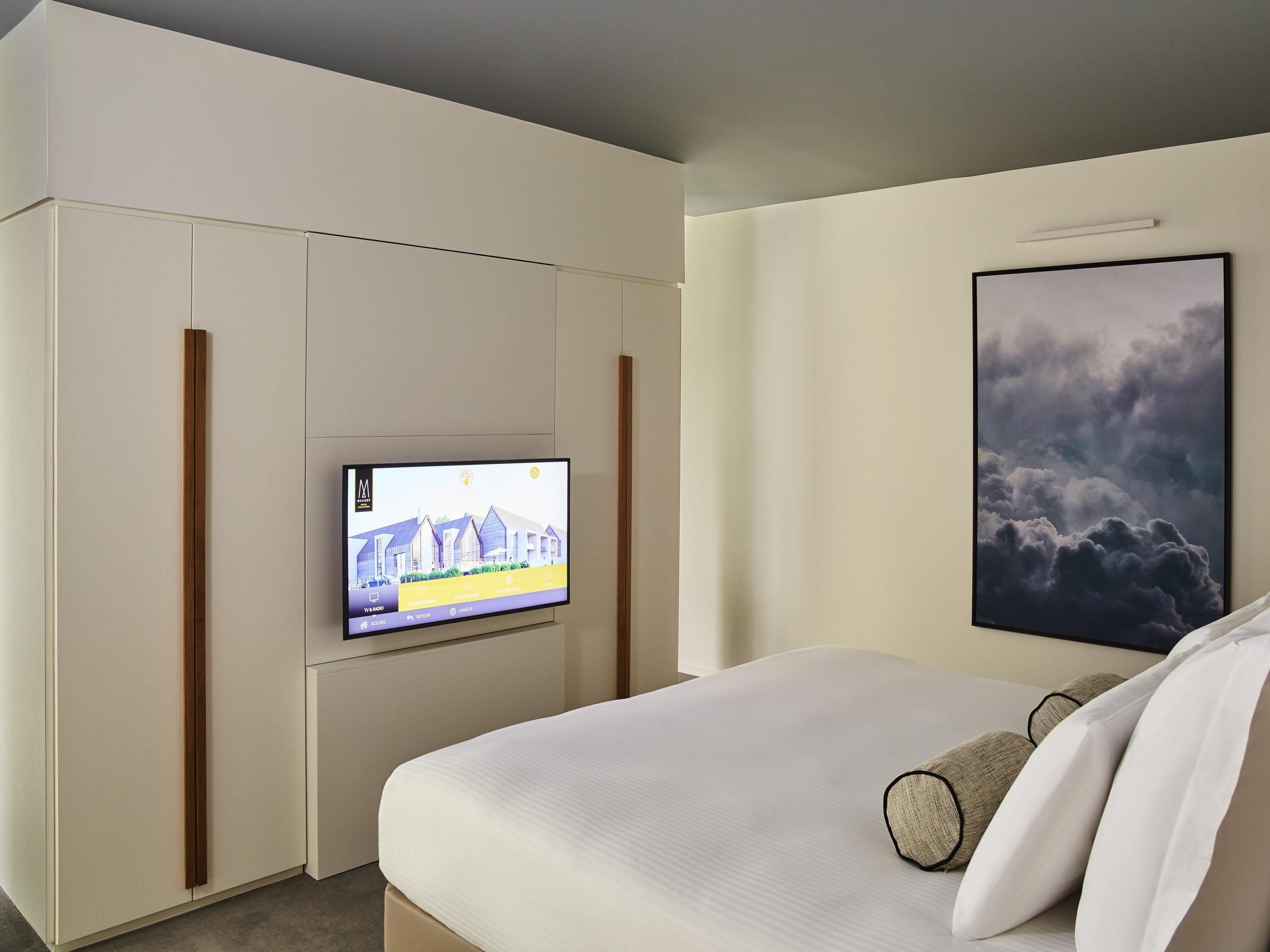 Una habitación de hotel con una cama, un televisor en la pared y un cuadro colgado sobre la cama.