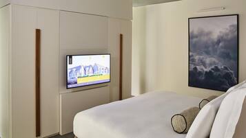 Una habitación de hotel con una cama, un televisor en la pared y un cuadro colgado sobre la cama.