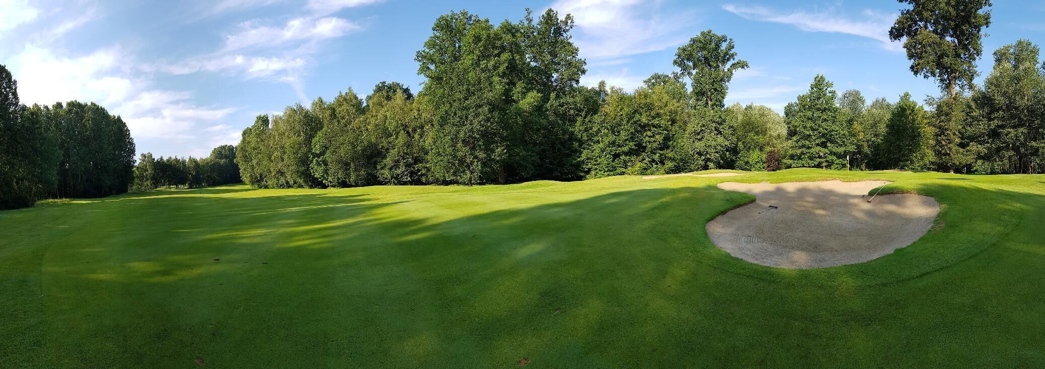 A golf course with a well-maintained green, sand bunkers, and dense trees in the background.