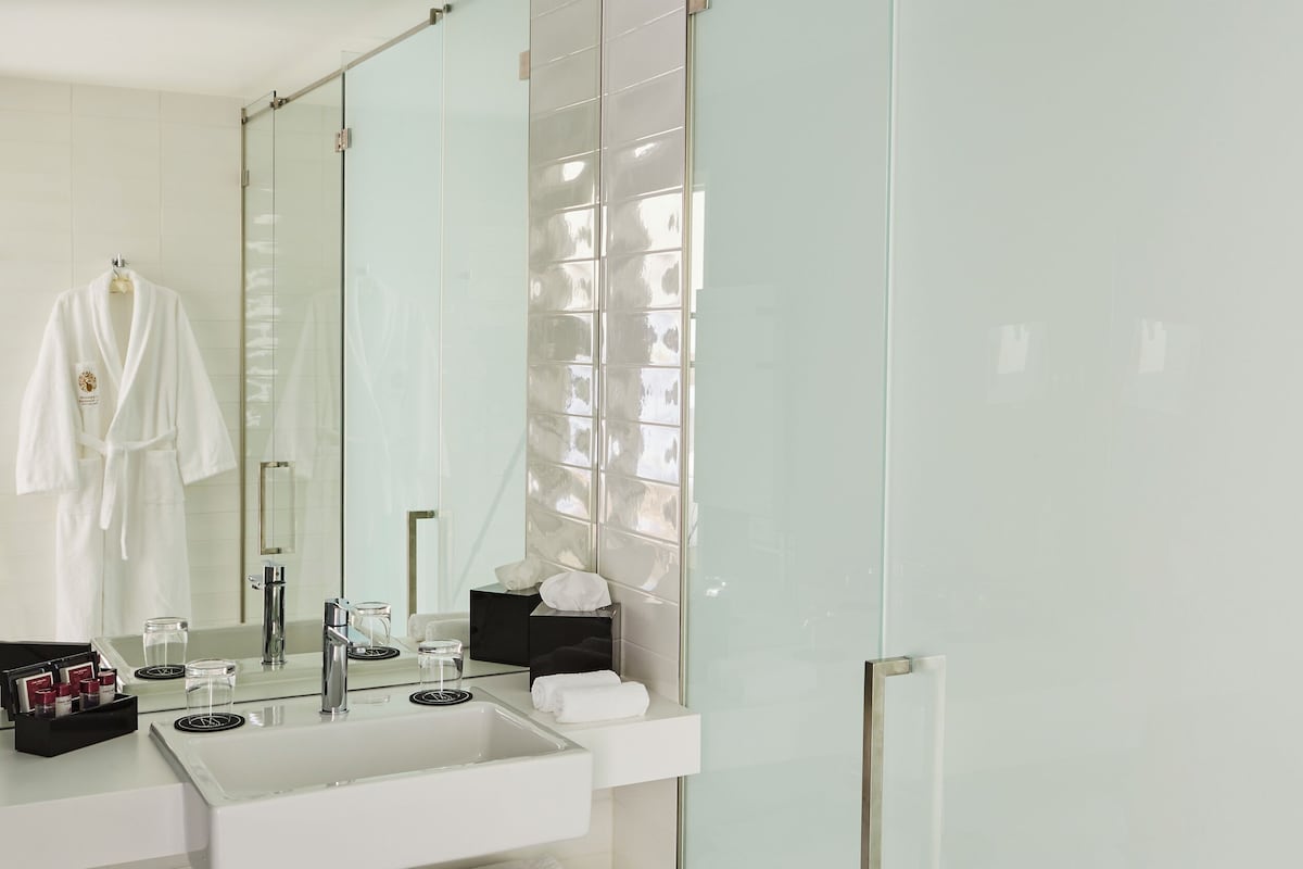 A modern bathroom with a large mirror, a white sink, a glass shower enclosure, and neatly folded towels on a shelf.