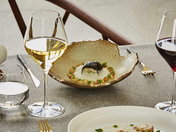 Une table à manger ornée d’un bol en céramique unique contenant un dessert, accompagné de verres à vin et de couverts.