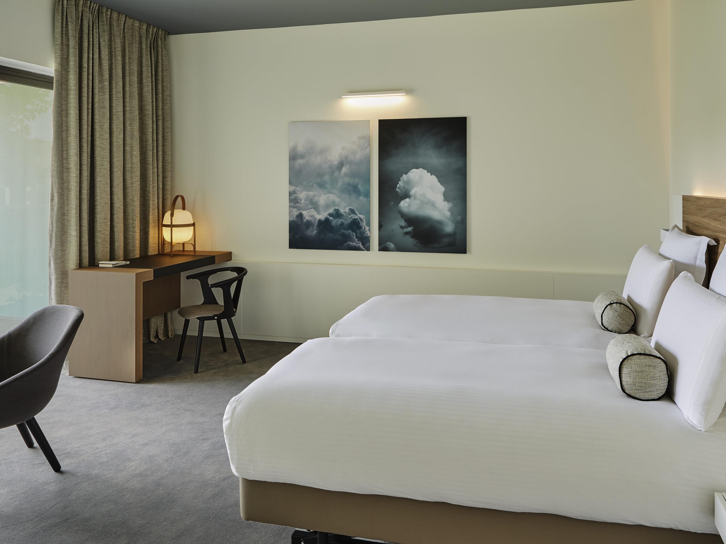 A hotel room with a bed, a desk, a chair, and two wall-mounted artworks.