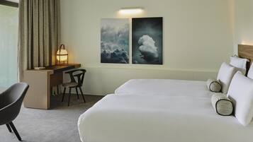 A hotel room with a bed, a desk, a chair, and two wall-mounted artworks.