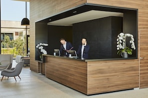 A reception desk with two staff members, a modern interior design, and a view of the outdoors. - Le Domaine des Vanneaux Golf & Spa L'Isle Adam - MGallery Collection (Presles)