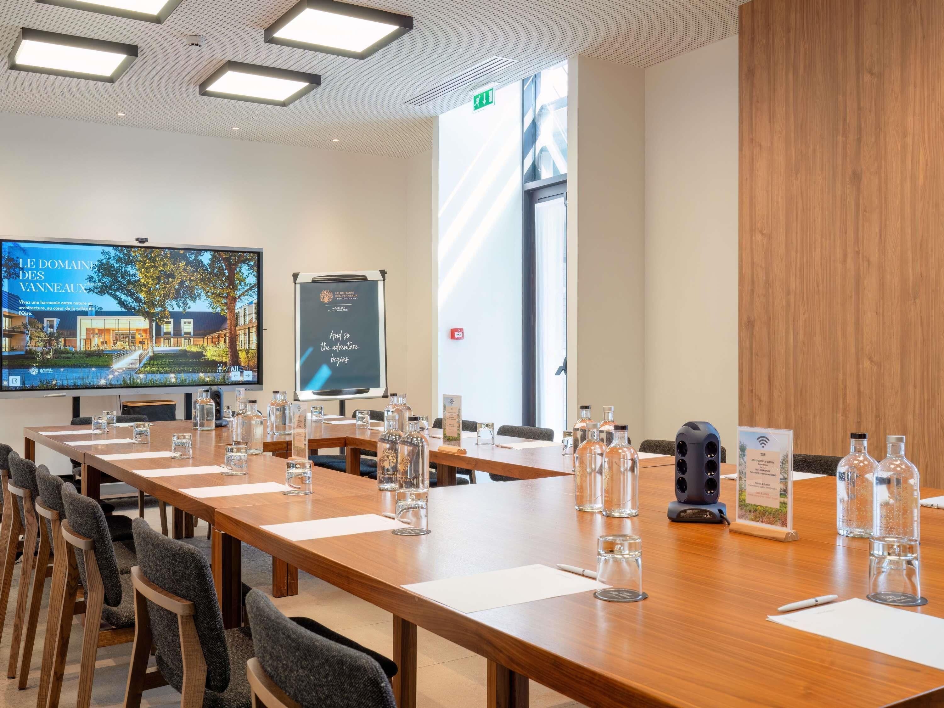 Une salle de conférence équipée d’une longue table, de chaises, d’un écran de projection et d’un tableau de présentation.
