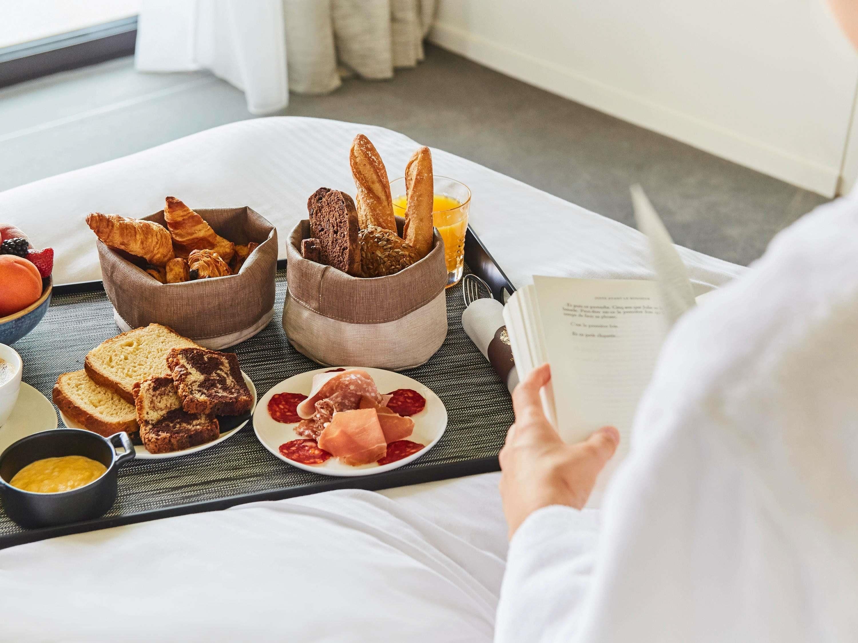 A breakfast tray with croissants, bread, pastries, and a glass of orange juice on a bed.