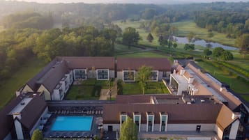 A modern hotel with a swimming pool, multiple buildings, and a golf course in the background.