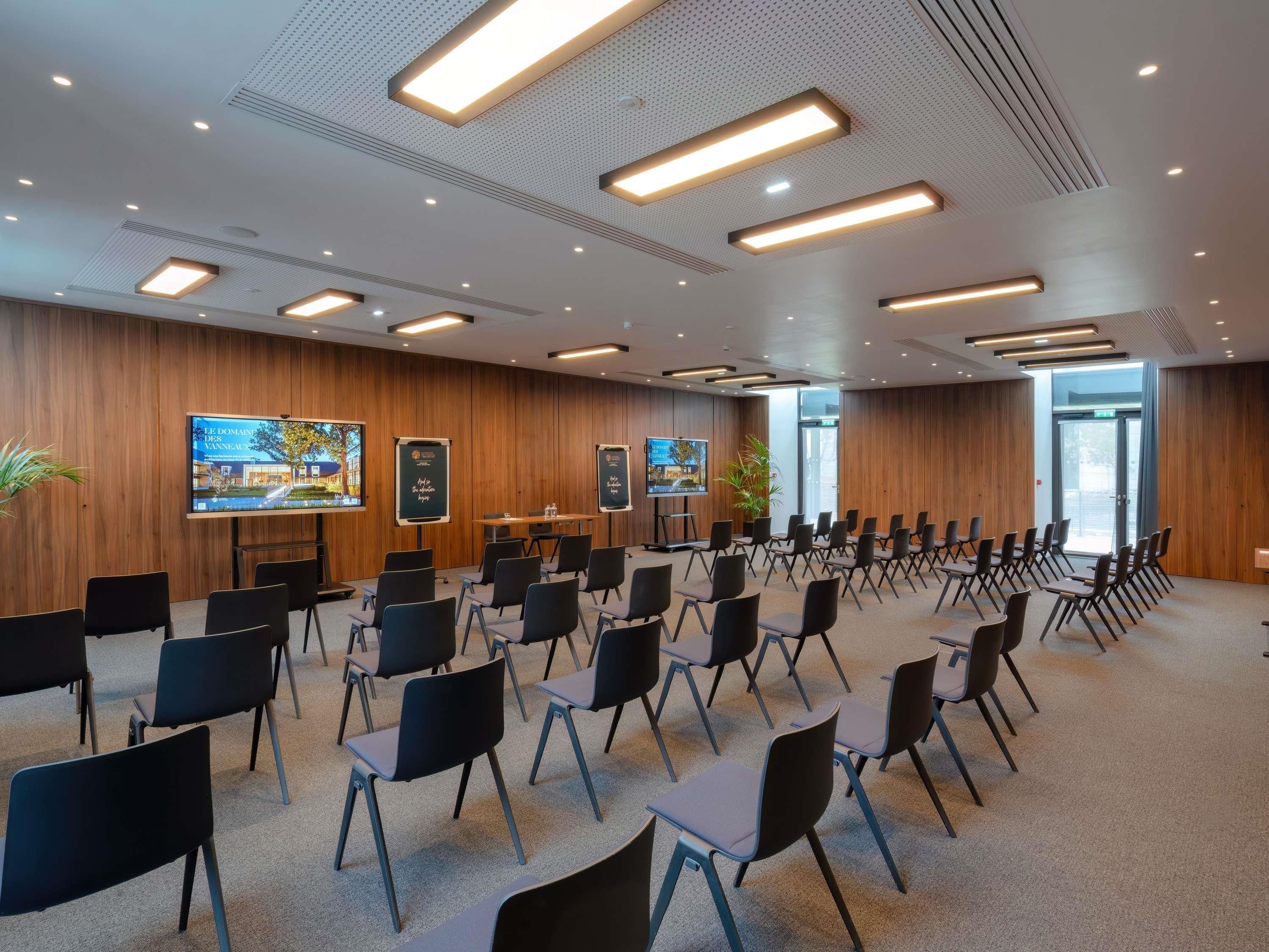 A conference room with rows of chairs, a large screen, and wooden panel walls.