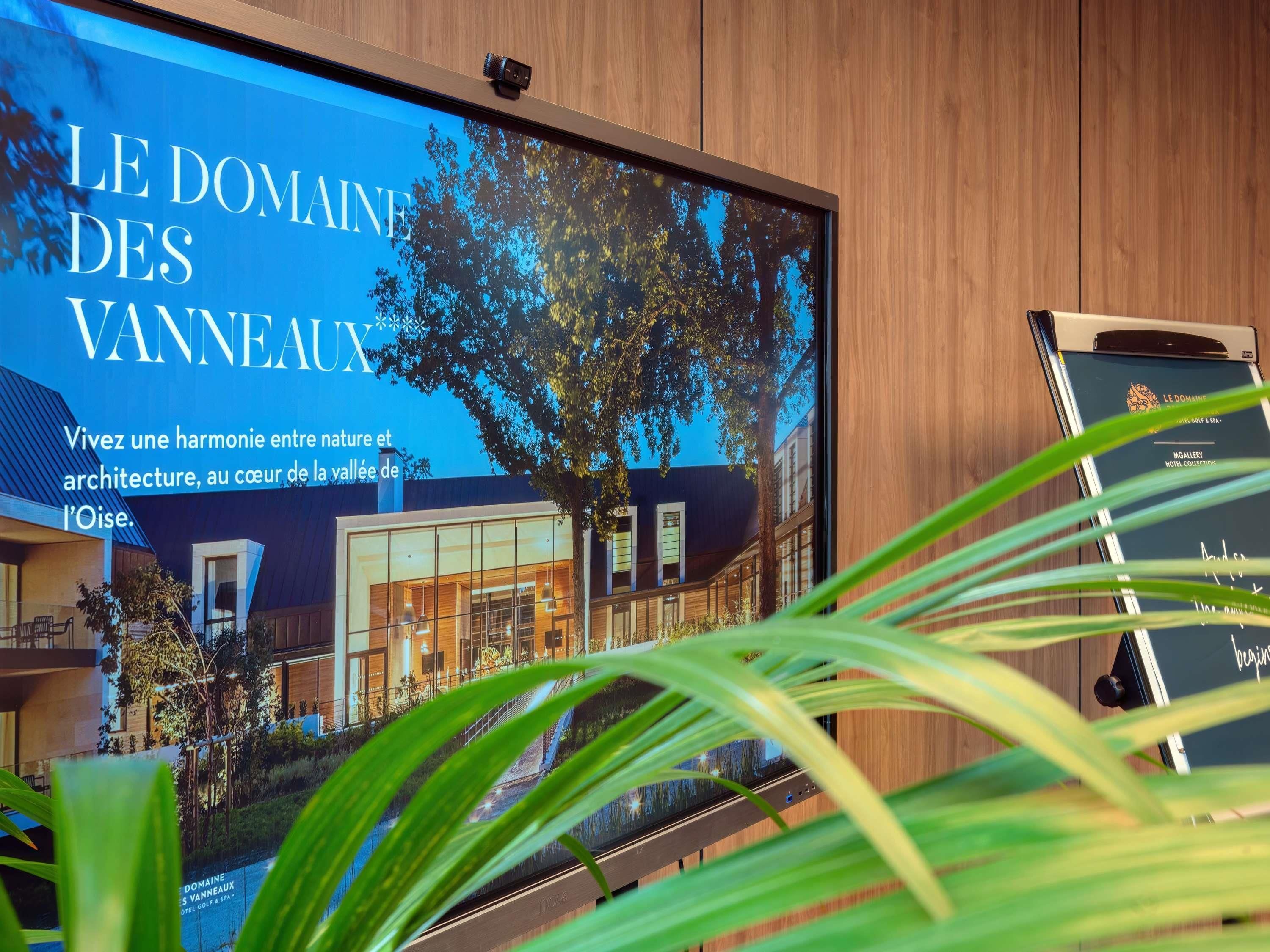 A modern hotel interior with a large digital display, wooden paneling, and indoor plants.
