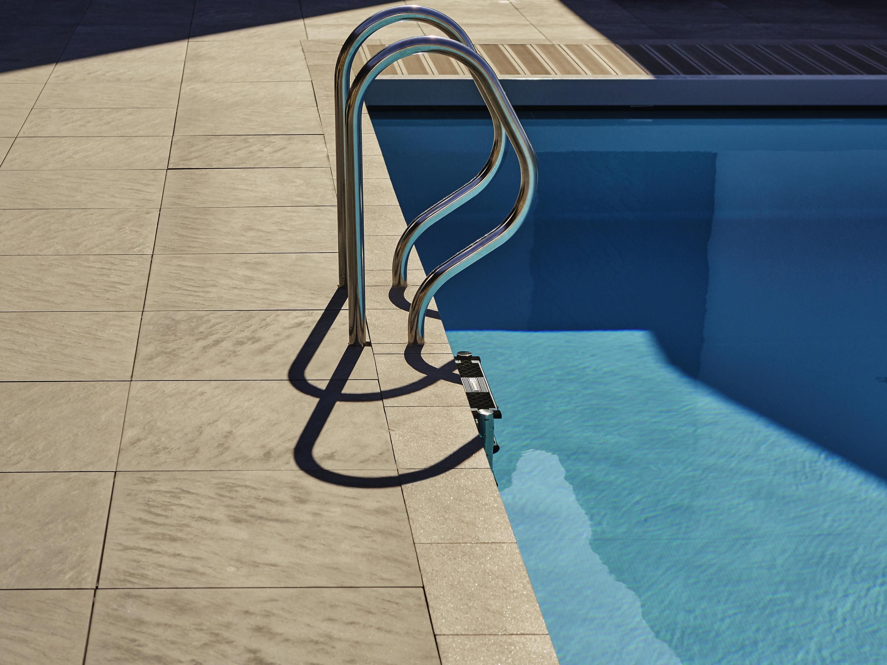 A swimming pool with a metal ladder and a tiled deck.