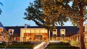 A modern building with large glass windows, a covered walkway, and a tree in the foreground. - Le Domaine des Vanneaux Golf & Spa L'Isle Adam - MGallery Collection (Presles)
